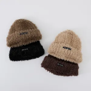 Flat lay of four colorful plush knitted beanies in brown, camel, beige, and black colors