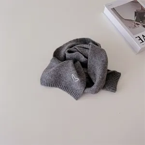 Détail d'une écharpe en tricot gris avec une broderie délicate en forme de cœur