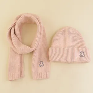 Detail of pink knitted hat and scarf set featuring ribbed texture and bear embroidery