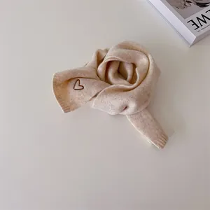 Détail d'une écharpe en maille beige avec broderie cœur et texture côtelée douce