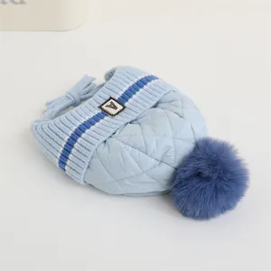 Dettaglio del cappello trapuntato azzurro per neonati con toppa A e grande pompon di pelliccia