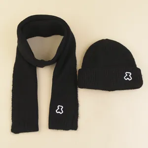 Detail of black knit beanie and scarf set with white embroidered bear logo on ribbed fabric