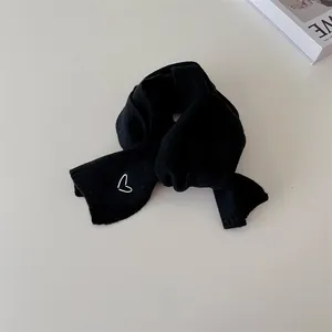 Détail de l'écharpe en tricot noir avec broderie de cœur blanc au style minimaliste