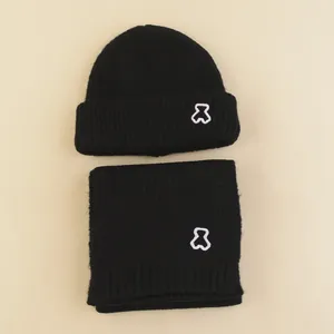 Detail of black knitted beanie and scarf set with white embroidered bear logo