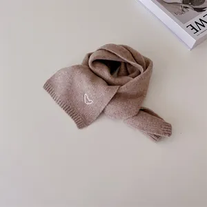 Gros plan de l'écharpe en tricot camel avec broderie coeur blanc et bords côtelés