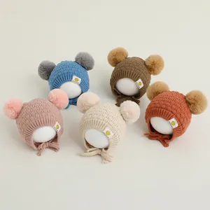 Detalle de cinco gorros de punto para bebé con pompones dobles y protección para orejas