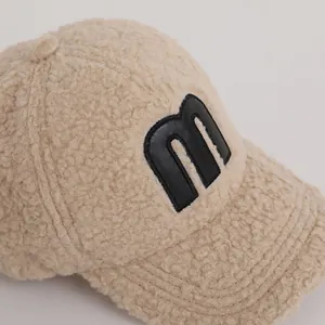 Close-up of warm beige fleece baseball cap with leather M patch and fuzzy texture
