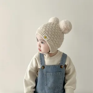 Detalle de gorro de punto para bebé con dos pompones de pelo sintético y orejeras crema