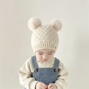 Detalle de gorro de punto para bebé con pompones dobles y textura de hilo crema