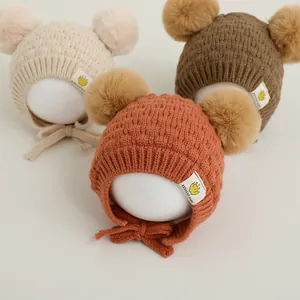 Detalle de tres gorros de punto para bebé con pompones dobles y correas de sujeción