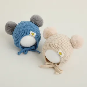 Detalle de gorro de punto para bebé con dos pompones, orejeras y correas suaves