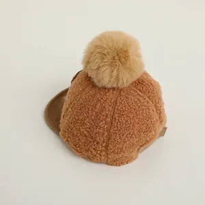 Detailed view of brown baby baseball cap with soft teddy fleece and plush pom-pom decoration