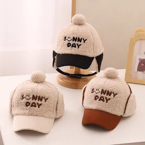 Detail of plush earflap hats with 'SUNNY DAY' embroidery and pom-poms for children