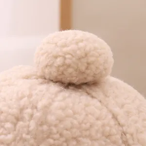Detailed close-up of soft beige faux shearling texture and plush pom-pom on the winter cap