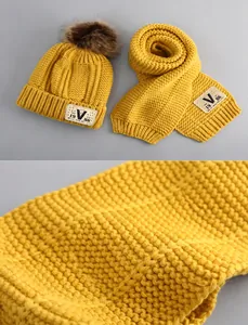 Detail of warm yellow knitted baby hat and scarf set with thick texture and V-logo patch