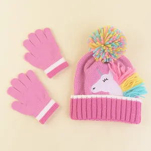 Close-up of pink knit baby hat with unicorn embroidery and colorful pom-pom details