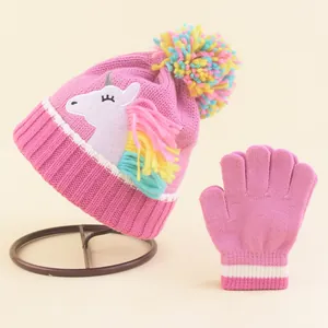 Close-up of pink knit baby hat and gloves set with unicorn patch and colorful pompom