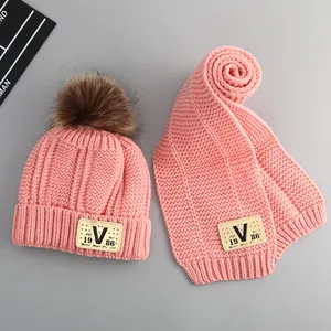 Detailed view of pink knitted baby hat and scarf set with brown faux fur pom poms
