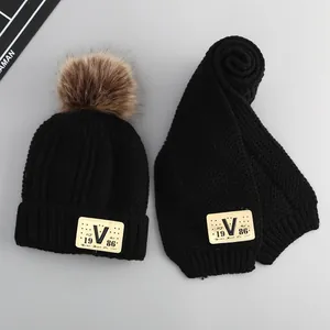 Detail of black winter knit hat and scarf set with V-patch and fluffy faux fur pompom