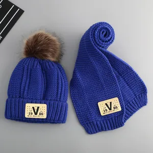 Close-up of blue knit beanie set with brown faux fur pompom and V-shaped leather patch