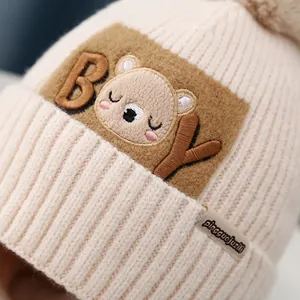 Detailed macro view of the cream-colored ribbed knit texture and cartoon bear patch on baby hat