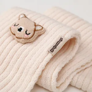 Detailed view of beige knit scarf featuring a cute bear patch and ribbed texture
