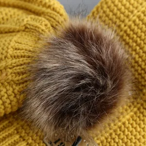 Ginger yellow knitted baby hat with a fluffy brown pom-pom and warm fleece lining