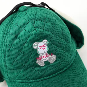 Detalle de gorra de béisbol acolchada verde con bordado de oso blanco y textura de rombos