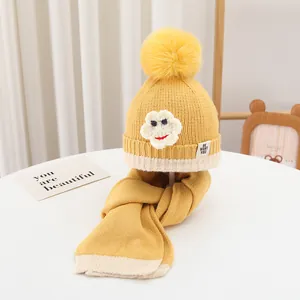 Detail der gelben Strickmütze mit flauschigem Bommel, weißer Blume und Smiley-Stickerei