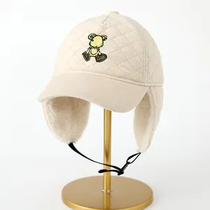 Detalle del gorro de invierno acolchado beige con bordado de oso y forro de vellón