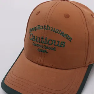 Detailed view of caramel brown baseball cap with green embroidery and contrast piping