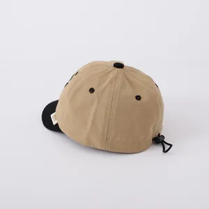 Detail of adjustable drawstring toggle on beige baseball cap with black visor and brim label