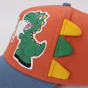 Detail of children's orange baseball cap featuring green cartoon dinosaur embroidery