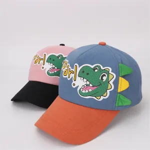 Detail of kids baseball caps featuring a green cartoon dinosaur print and 3D decorative fins