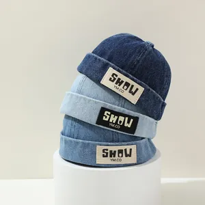 Three denim beanies for kids in dark and light blue shades with woven logo labels