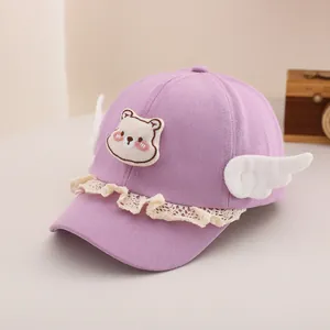 Détail du bonnet violet pour bébé avec écusson ours, dentelle et ailes 3D blanches