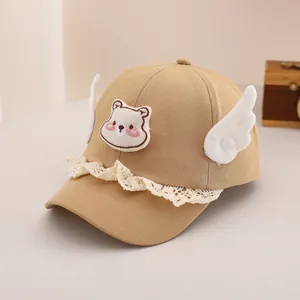 Détail d'une casquette bébé avec écusson ours, ailes en peluche et bord en dentelle