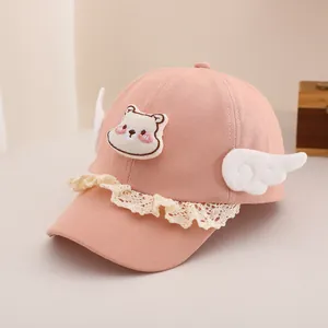 Détail d'une casquette rose pour bébé avec broderie ours, dentelle et petites ailes blanches
