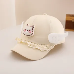 Détail de casquette bébé avec broderie ours, bordure en dentelle et ailes mignonnes