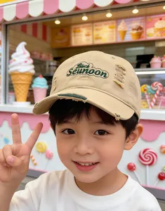 Détail des lettres brodées vertes et des bords effilochés sur une casquette beige pour enfants