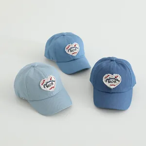 Detailed view of three denim baseball caps with heart patch embroidery in various blue tones
