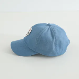 Detail of light blue denim baseball cap showing heart embroidery and fabric texture