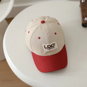 Detail of embroidered L.DO SURPRISE patch on beige and red kids baseball cap