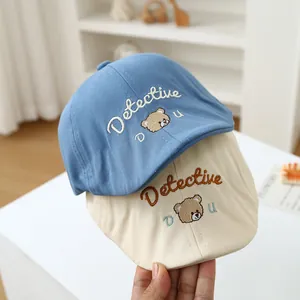 Detail of blue and beige cotton baby beret hats with bear embroidery and lettering