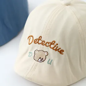 Detailed close-up of bear and Detective embroidery on the cream baby beret hat