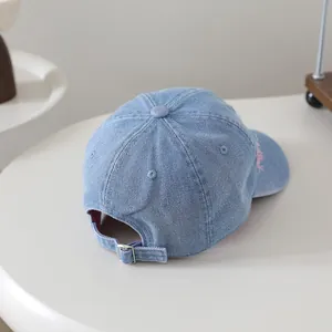 Detail view of light blue washed denim baseball cap with metal buckle and pink embroidery