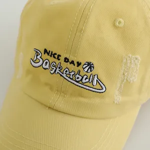 Detailed close-up of embroidered letters and vintage distressed holes on a yellow cotton cap