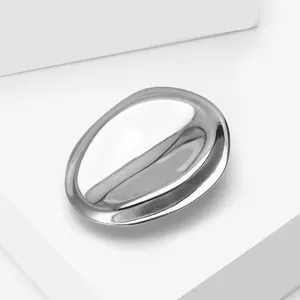 Detailed close-up of a silver geometric brooch with a polished mirror finish on white blocks