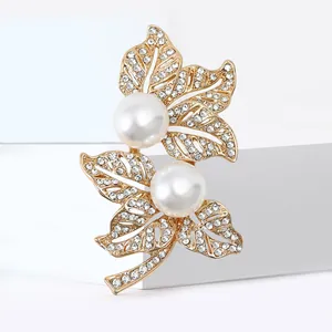 Spilla a foglia dorata con perle bianche e strass scintillanti su piedistallo bianco