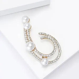 Close-up of golden brooch with hollow design featuring white pearls and sparkling rhinestones